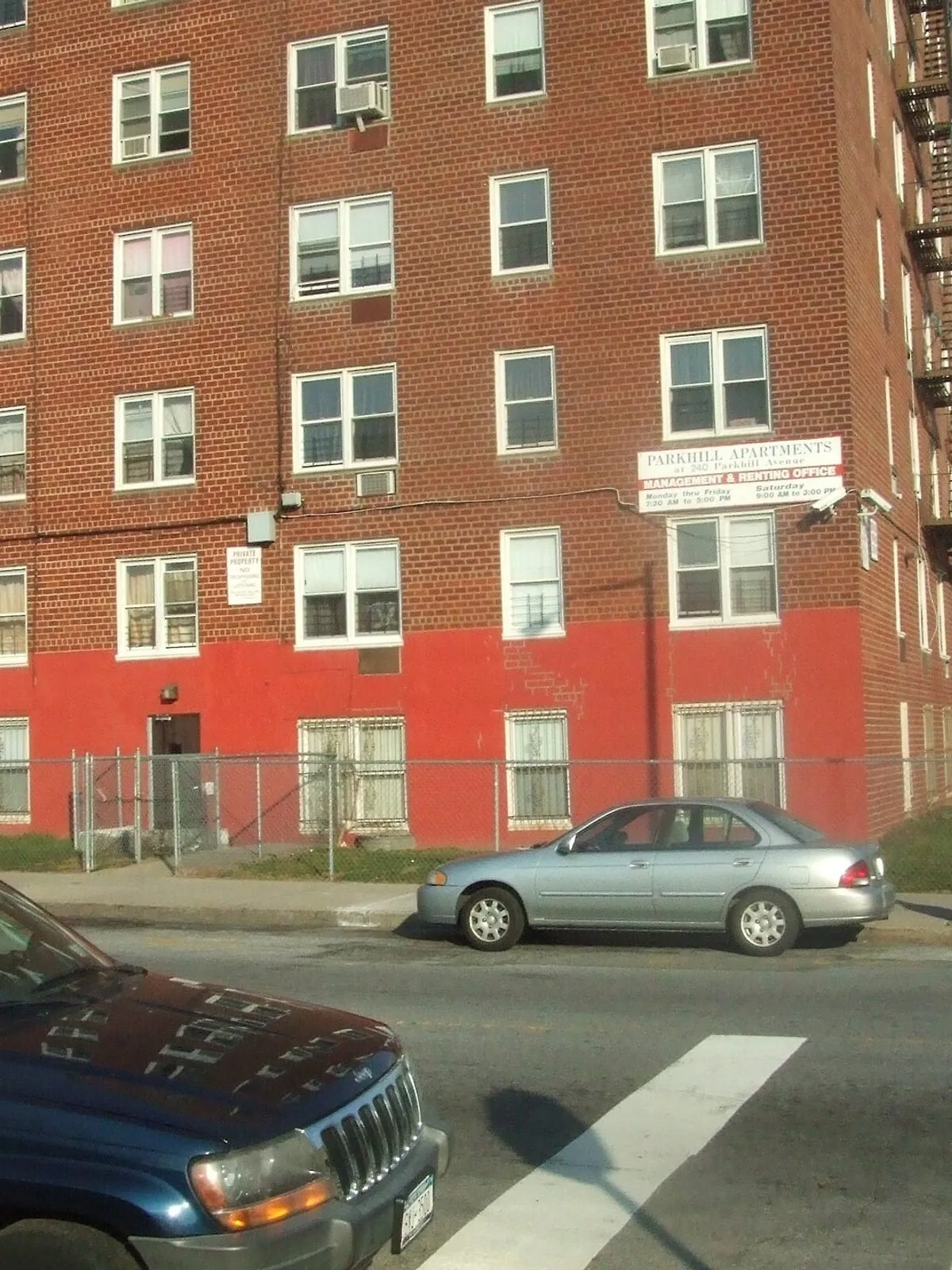 Occupied brick apartment block on a New York corner, fire escapes running down the street elevation.