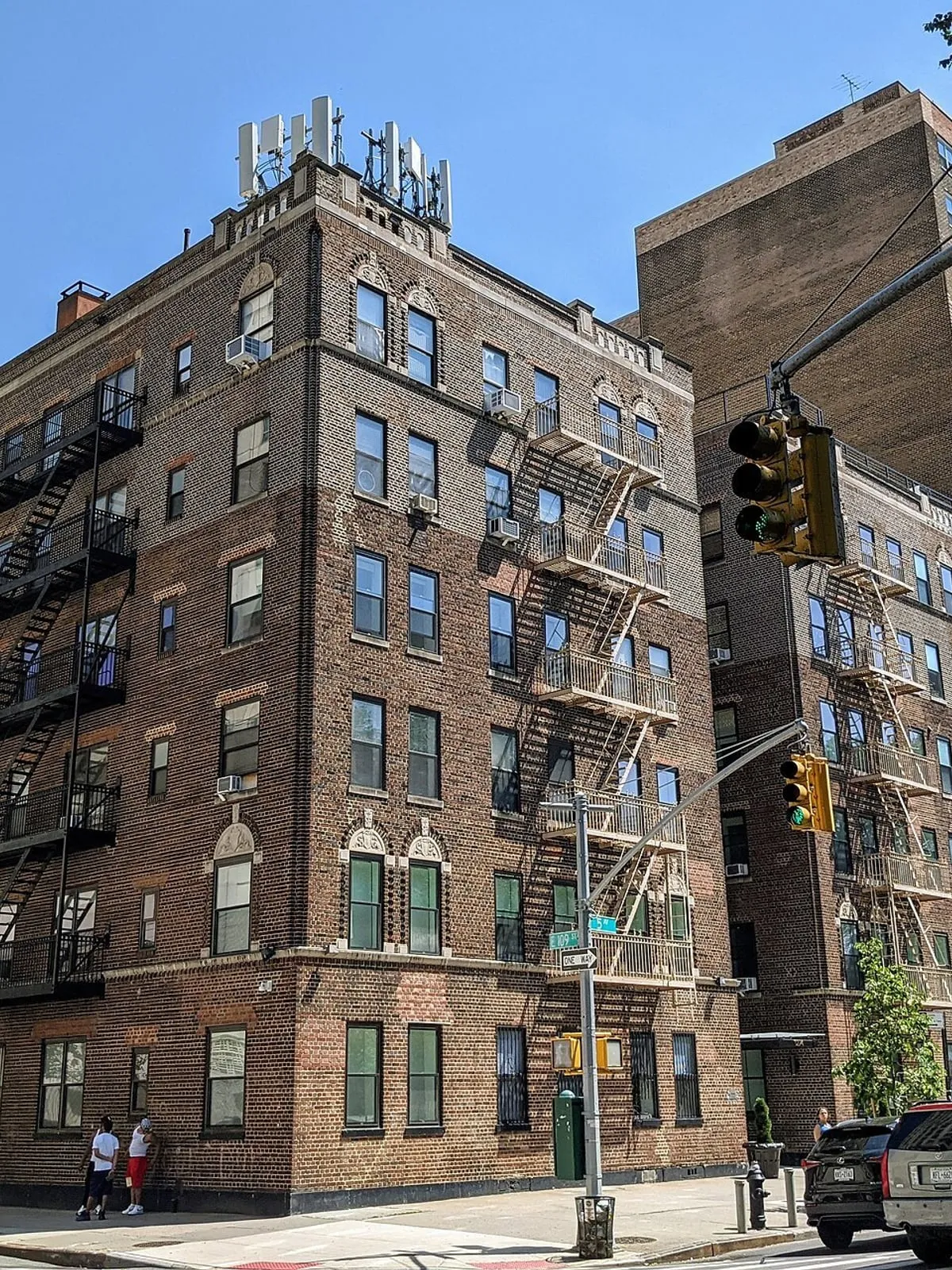 Pre-war brick apartment building on the corner of Fifth Avenue, fire escapes stacked up the side elevation.