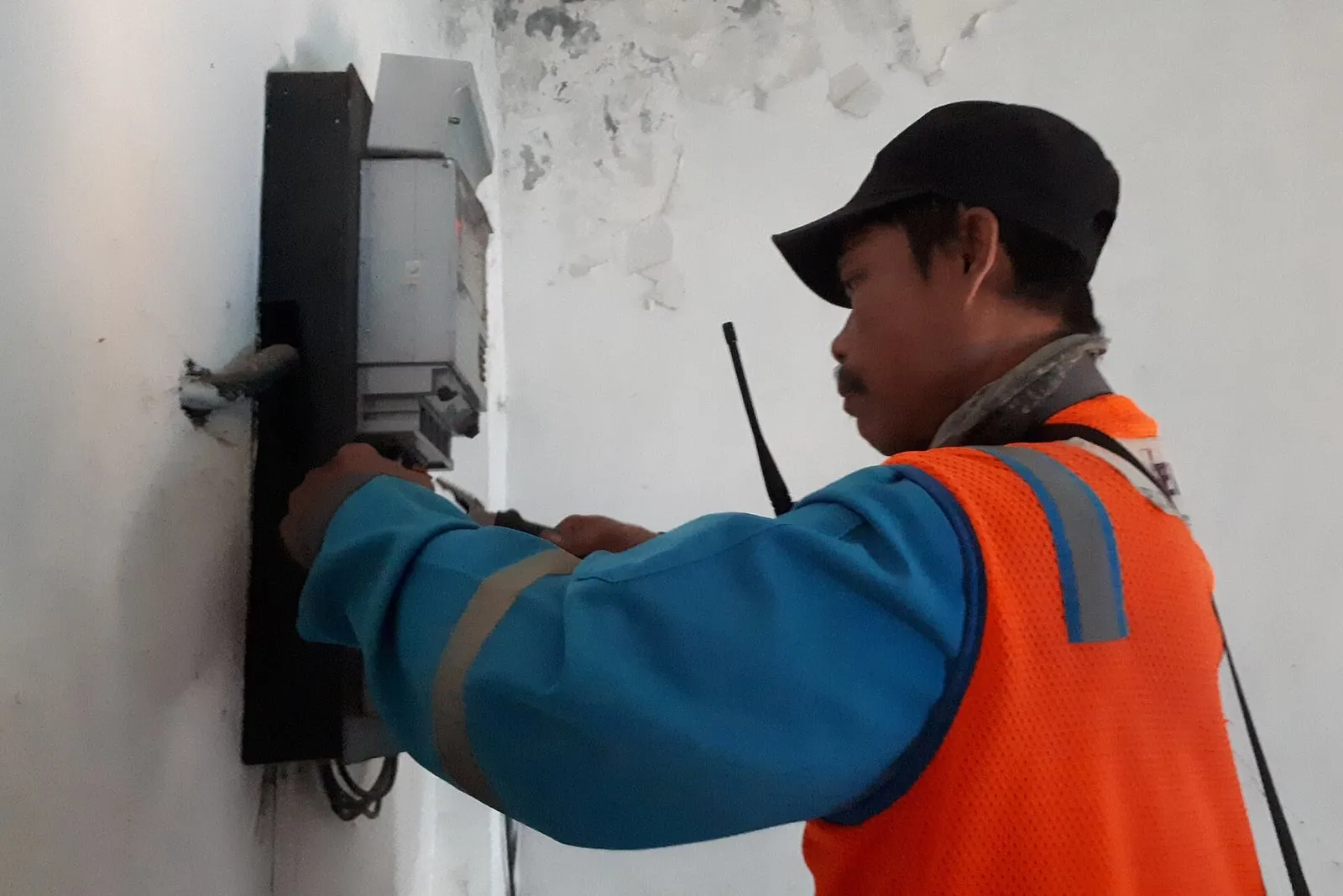 Electrician in hi-vis working inside an open meter cabinet, radio clipped to his shoulder.