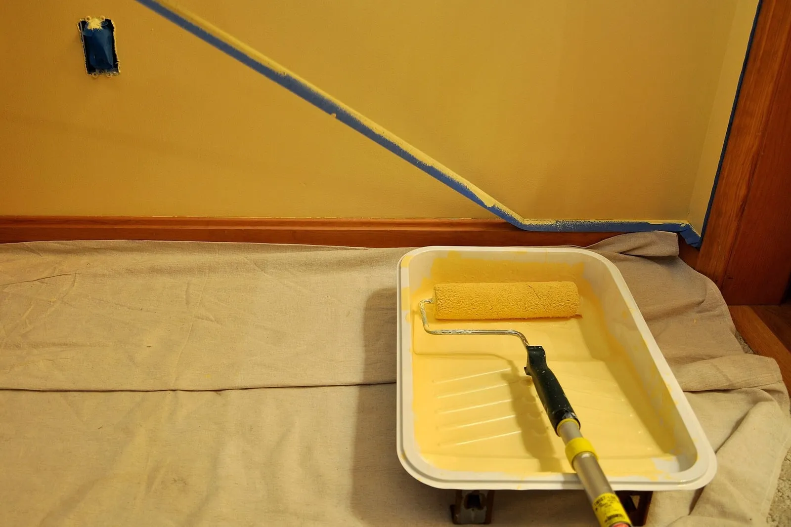 Roller and tray set down on a drop cloth mid-way through repainting a room.