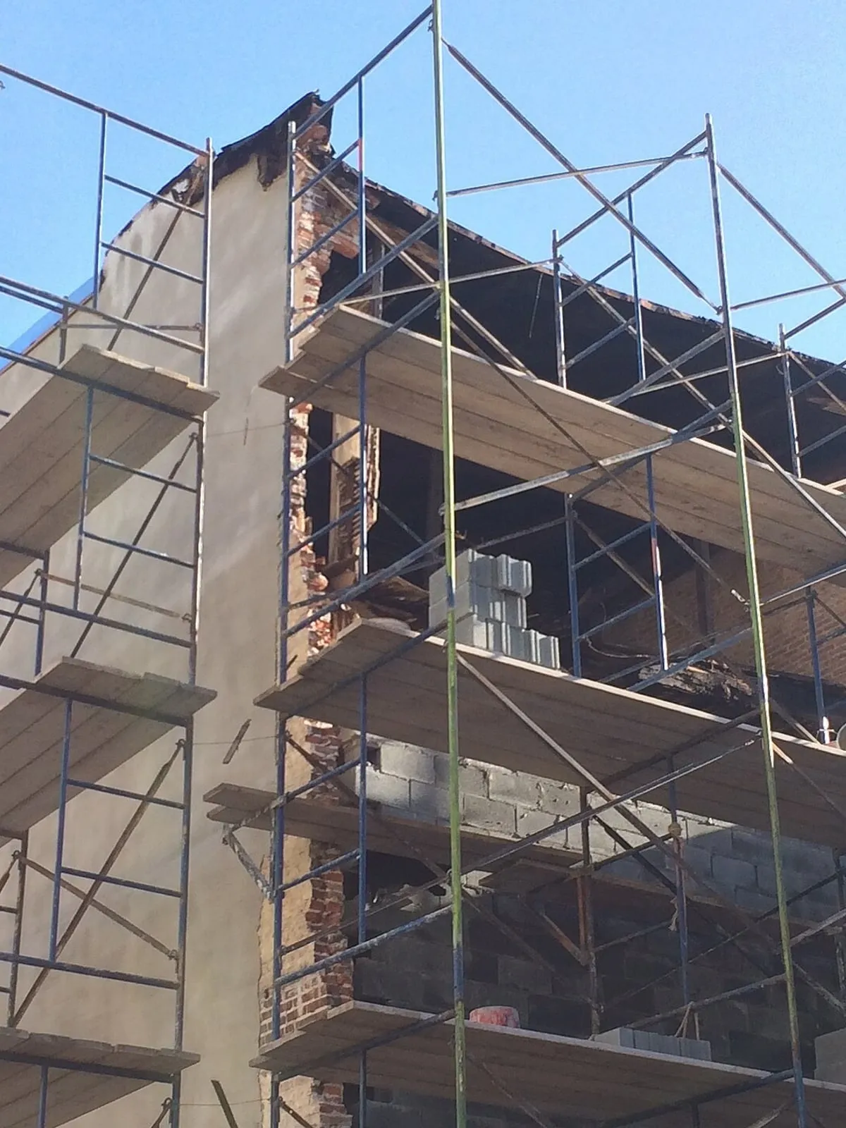 Scaffold standing the full height of a brick building's rear elevation while the wall behind it is repaired.