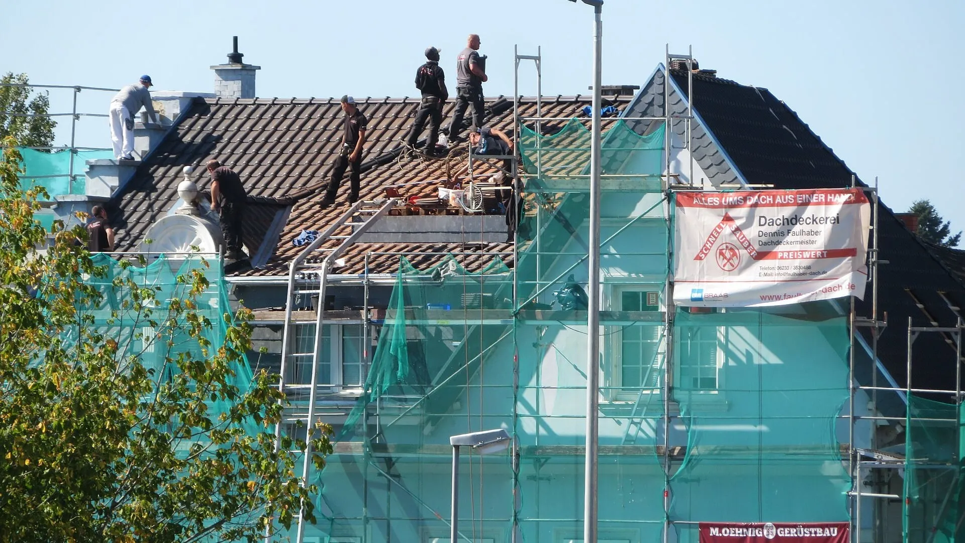 Re-roofing crew working across a scaffolded roof, tiles stripped back to the battens.