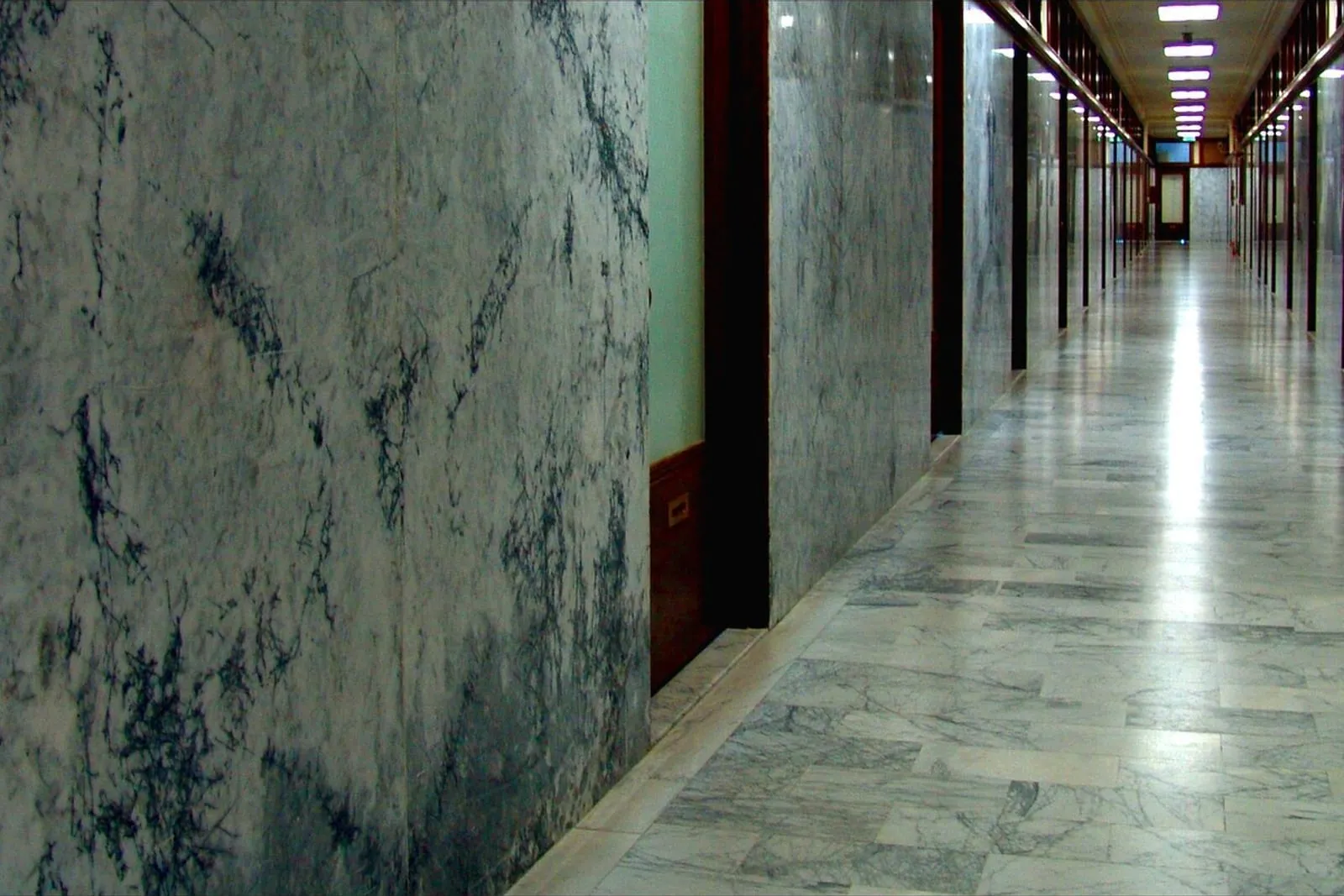 Long stone-clad corridor running the length of a building floor, doors set into both walls.