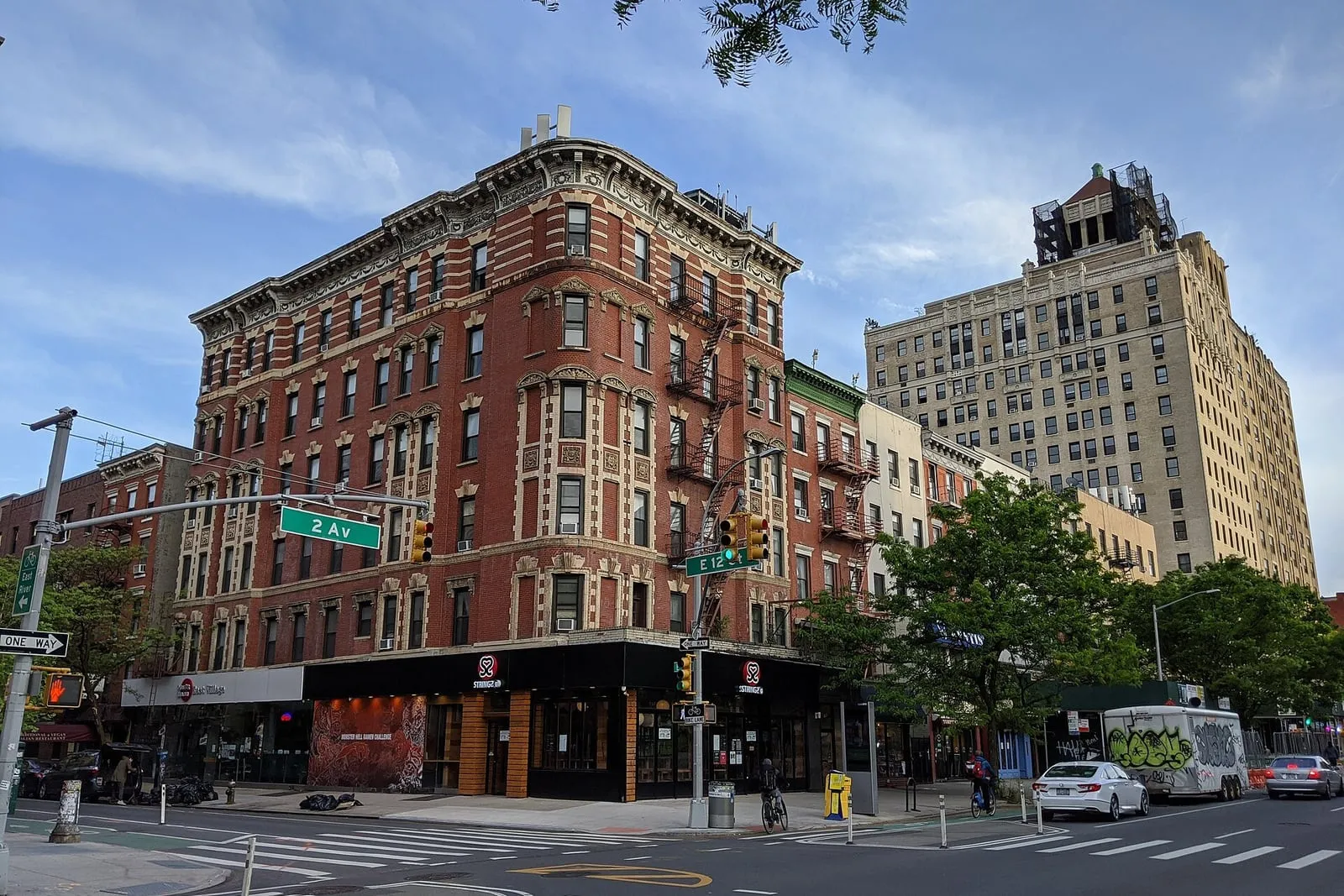 Pre-war brick apartment building on a Manhattan corner, fire escapes and storefronts along Second Avenue.